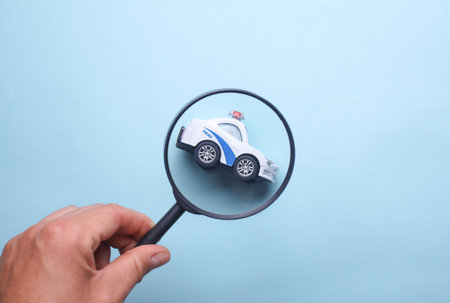Hand looking through magnifying glass at toy police carの写真素材