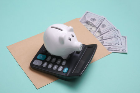 Envelope with hundred dollar bills and calculator, piggy bank on blue background. Paying taxesの写真素材