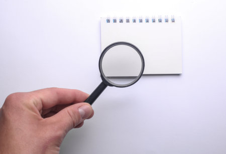 Hand with a magnifying glass examines blank notebook