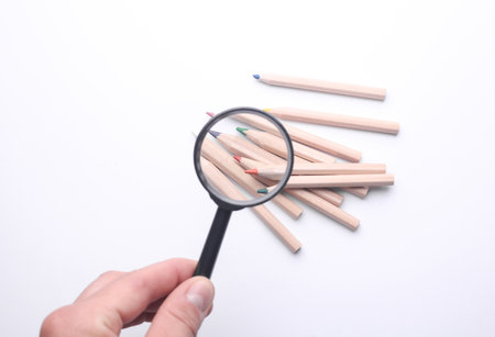 Hand with a magnifying glass examines colored pencils