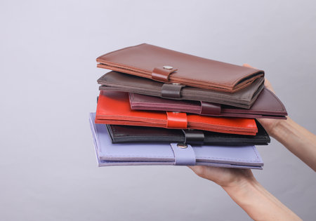 Hands holding stack of leather document organizer folders on gray background