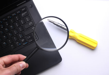 Hand with a magnifying glass examines laptop. Search for breakdowns