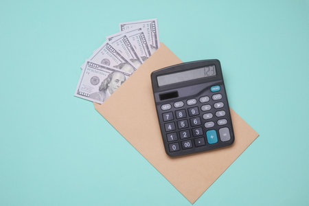 Envelope with hundred dollar bills and calculator on blue background. Paying taxesの写真素材