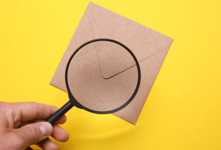 Hand with a magnifying glass examines envelope on yellow background