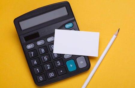 Calculator with business card and pencil on yellow backgroundの写真素材