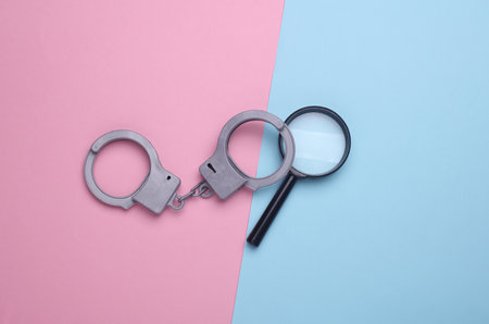 Handcuffs with magnifying glass on blue pink backgroundの写真素材