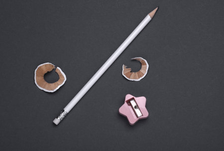 White sharpened pencil and shavings with sharpener on dark gray backgroundの写真素材