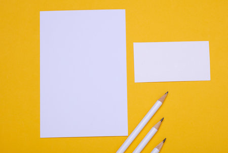White blank card with paper sheet and pencils on yellow backgroundの写真素材