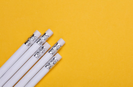 White wooden pencils with erasers on yellow background. Mockup for designの写真素材