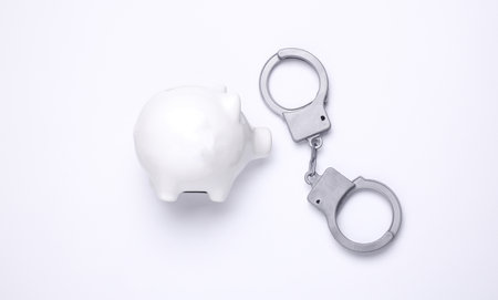 Piggy bank and toy plastic handcuffs on white background. Illegal encumbrance, corruption