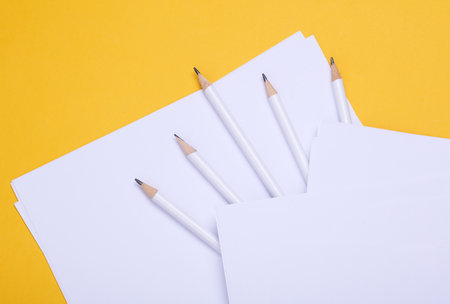 Pencils with white blank sheets of paper on yellow background