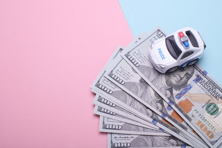 Hundred dollar bills and toy police car on blue pink background. Corruption, crime, justice conceptの写真素材