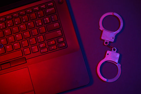 Laptop with handcuffs in neon light. Cyber ââpoliceの写真素材