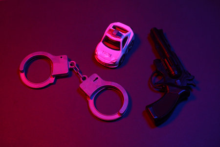 Toy handcuffs and police car, gun in red blue neon lightの写真素材