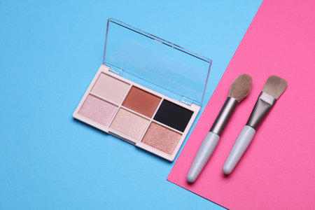 Makeup eyeshadow palette and brushes on blue pink background