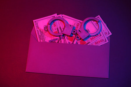 Envelope with hundred dollar bills and handcuffs in red blue neon light. Corruption, crime