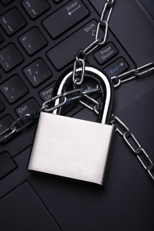 Laptop wrapped with steel chain and lock on dark backgroundの写真素材