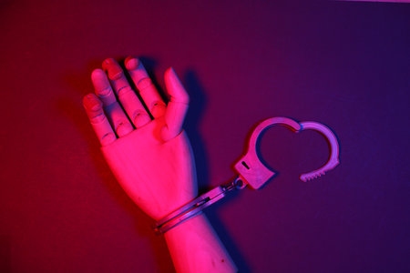 Handcuffs are put on a wooden puppet's hand in red and blue neon light. Crime and Justice
