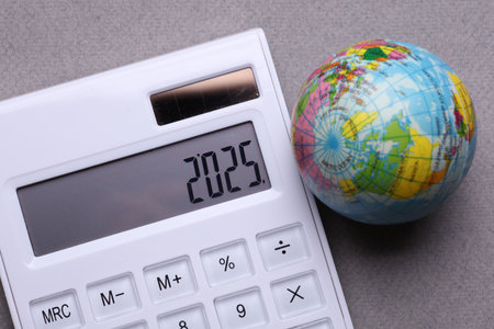 Calculator with number 2025 and globe on gray background. Economic analysis, budget of the year
