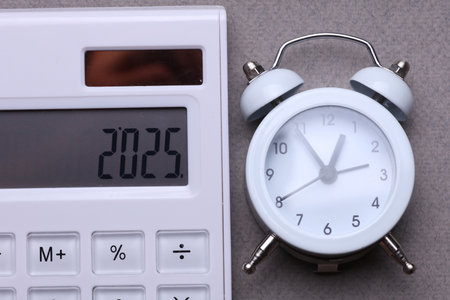 Calculator with number 2025 and alarm clock on gray background. Economic analysis, budget of the yearの写真素材