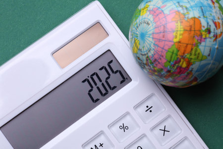 Calculator with number 2025 and globe on green background. Economic analysis, budget of the yearの写真素材