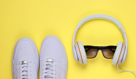 White Sneakers and headphones with sunglasses on yellow background. Casual design. Music concept. Flat lay, minimal.の写真素材