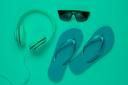 Accessories for relaxing on the beach. Flip flops, headphones, sunglasses. Studio shot in green neon light. Top viewの写真素材
