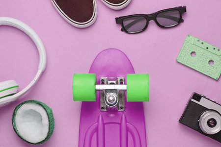 Hipster outfit. Skateboard with headphones, audio cassette, retro camera and sneakers on pink background. Creative fashion minimalism. Minimal summer fun. Pop art. 80s.の写真素材