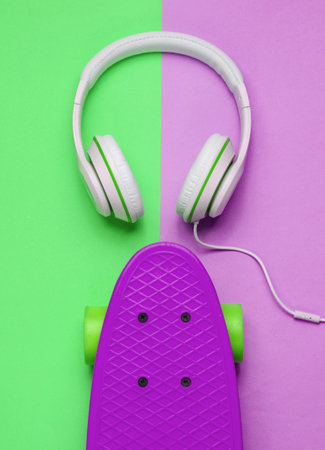 Hipster outfit. Skateboard with headphones on colored pastel background. Creative fashion...