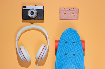 Hipster outfit. Skateboard with headphones, audio cassette on yellow color background. Creative fashion minimalism. Trendy retro 80s style. Minimal summer fun. Music concept. Top viewの写真素材