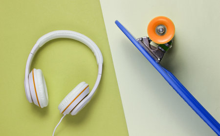 Hipster outfit. Skateboard with headphones on colored background. Creative fashion minimalism....