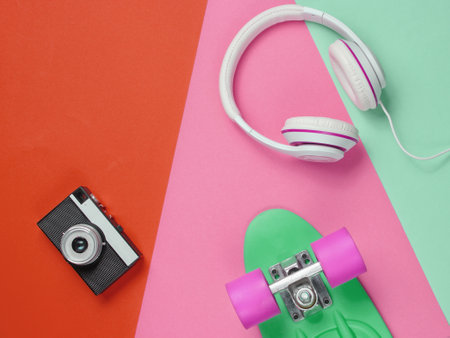 Hipster outfit. Skateboard with headphones, retro camera on colored background. Creative fashion...