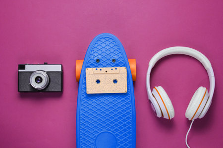 Hipster outfit. Skateboard with headphones, retro camera, audio cassette on purple background....