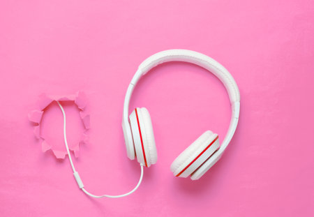 White classic wired headphones on pink background with a torn hole. Retro style. Minimalistic music concept. Top view.の写真素材