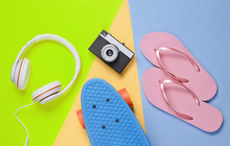 Hipster outfit. Skateboard with headphones, flip flop, retro camera on colored background. Creative...