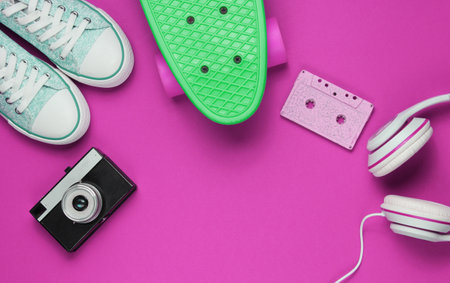 Hipster outfit. Skateboard, headphones, audio cassette, sneakers, retro camera on pink background. Creative fashion minimalism. Minimal summer fun. Pop art. 80s. Copy space. Top viewの写真素材