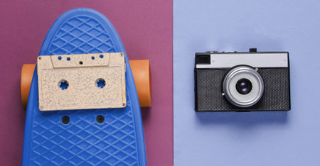 Retro set with blue skateboard with audio cassette and retro camera on colored background. Studio...