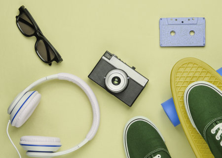 Hipster outfit. Skateboard with headphones, audio cassette, retro camera and sneakers on green pastel background. Creative fashion minimalism. Minimal summer fun. Top viewの写真素材