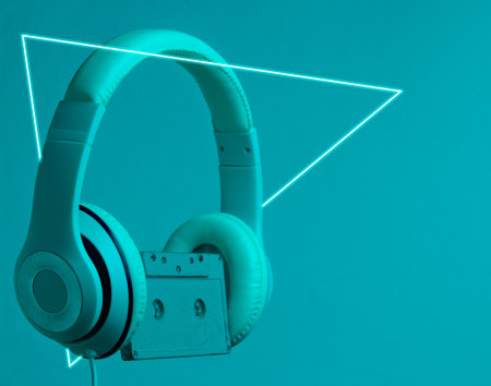 Retro wave. Headphones and audio cassette in neon light with a luminous led triangle. 80s