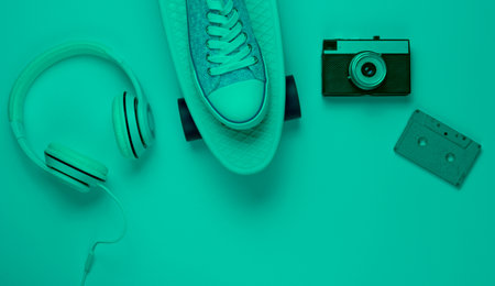 Hipster outfit. Skateboard, headphones, audio cassette, sneakers, retro caamera in mint green neon light. Creative fashion minimalism. Minimal summer fun. Pop art. 80s. Copy space. Top viewの写真素材