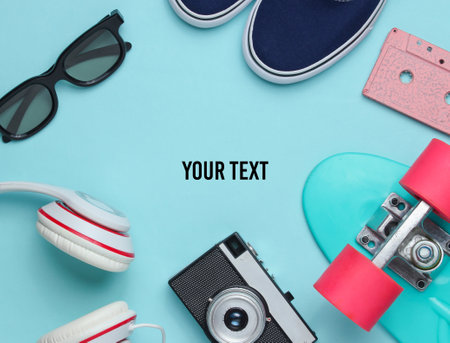 Hipster outfit. Skateboard with headphones, audio cassette, retro camera and sneakers on blue background. Creative fashion minimalism. Minimal summer fun. Pop art. 80s. Copy space.の写真素材