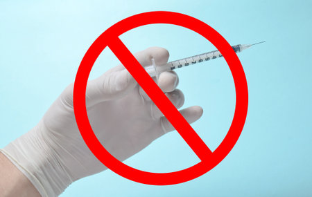 Vaccination ban. Medic's hand with white latex gloves holds syringe with needle on blue background with prohibition sign. Medical conceptの写真素材