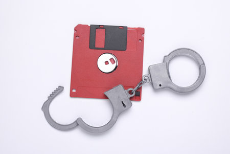 Floppy disk with handcuffs on white background. Cyber crimes