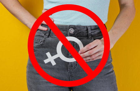 Femen concept. Woman holds in her hands gender feminism symbol on yellow background with prohibition sign. Crop photo, studio shotの写真素材