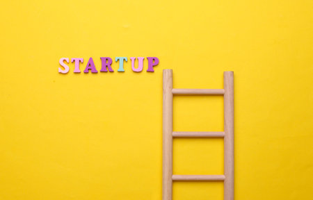 Wooden ladder and word startup on yellow background.の写真素材