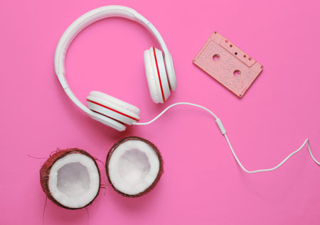 Music lover creative concept. Summer background. white classic headphones, retro audio cassette, coconut halves on pink background. Top viewの写真素材