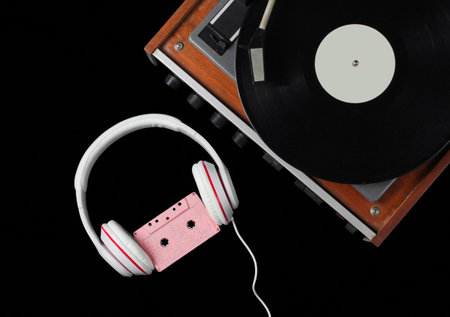 Retro style music concept. Classic headphones with audio cassette, vinyl record player on black...