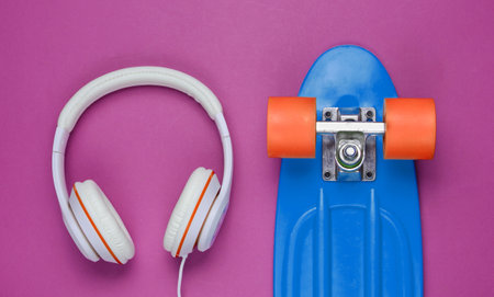 Hipster outfit. Skateboard with headphones on purple background. Creative fashion minimalism. Trendy...
