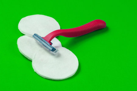 Beauty still life, minimalism. Plastic epilator razor with cotton circles on green background....