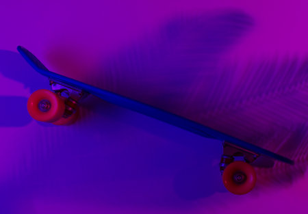 Plastic mini cruiser board on background with shadow from palm leaves. Neon gradient light. Top view